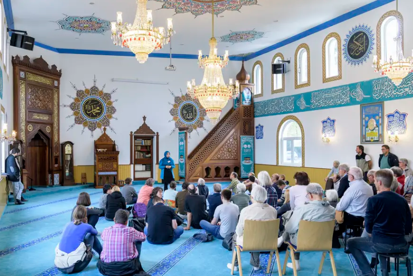Moscheeführung in der Yavuz Sultan Selim Moschee: Eine Gruppe von Besuchern im Gespräch mit der Führerin im Gebetsraum.